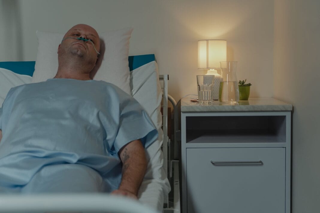 Mężczyzna leżący w szpitalnym łóżku z kaniulą donosową przy lampce Mężczyzna leżący w szpitalnym łóżku z kaniulą donosową przy lampce